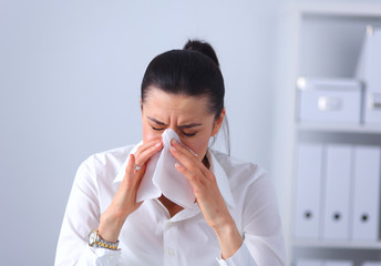 Young businesswoman blowing her nose, sits at the desk