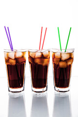 three glasses of cola with ice and straws on a white background.