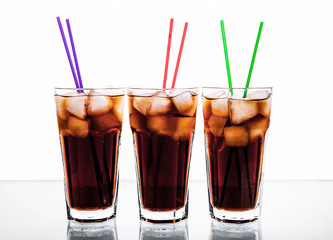 three glasses of cola with ice and straws on a white background.