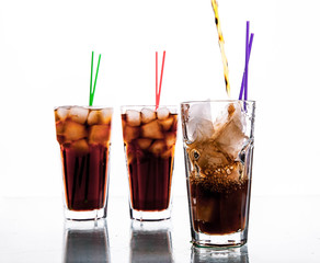 three glasses of cola with ice and straws on a white background.