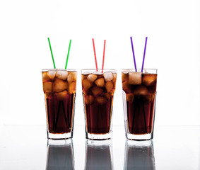 three glasses of cola with ice and straws on a white background.