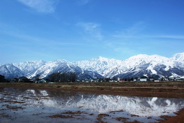 Fototapeta na wymiar 雪解け始まる春の風景/雪解け水に反射する雪山の風景です