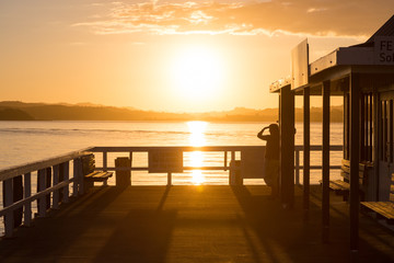A woman standing at a pier and looking into the distance at suns