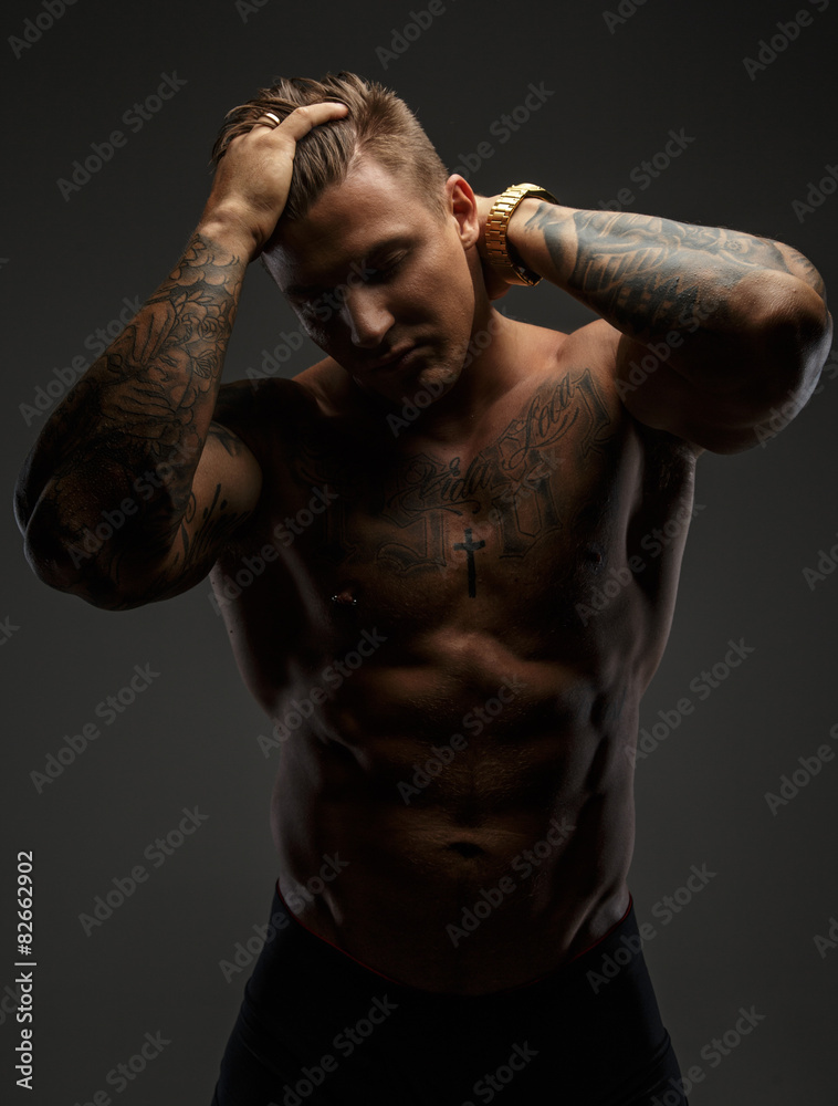 Wall mural Muscular man with tattooes in deep shadows