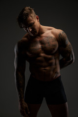 Fototapeta na wymiar Muscular man with tattooes in deep shadows