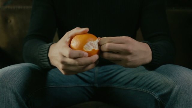Young man sitting on a sofa and peeling an orange 