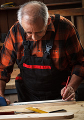 Fototapeta na wymiar Senior carpenter marking a measurement on a wooden plank