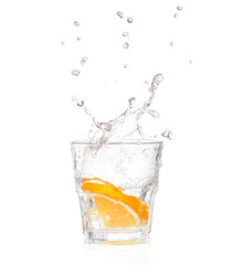 orange splashing into glass of water on white background