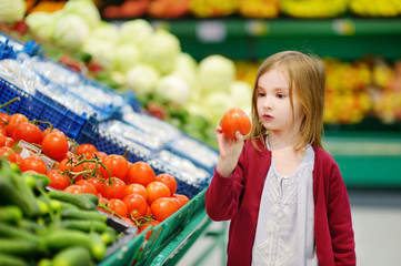 Little girl choosing tomatoes in a food store