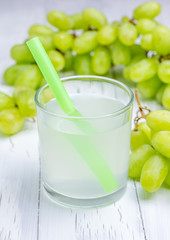 Glass of white grapes juice and grapes on background