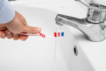 man brushing teeth with toothbrush under the sink water