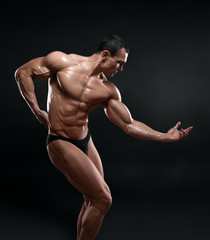 Handsome muscular bodybuilder posing over black background.