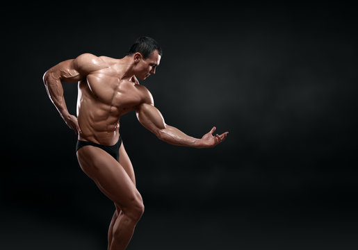 Handsome muscular bodybuilder posing over black background.