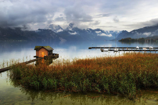 Pier at the Traunsee lake with old hut and boats in Alps mountai
