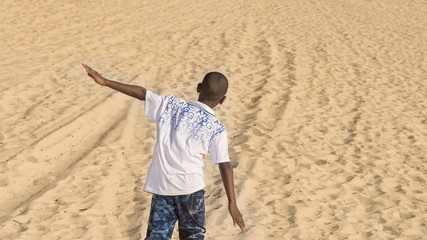 Afro boy walking in the sand, ten years old 