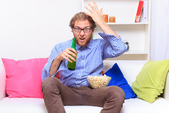 Dissatisfacted man with pocorn and beer on the couch