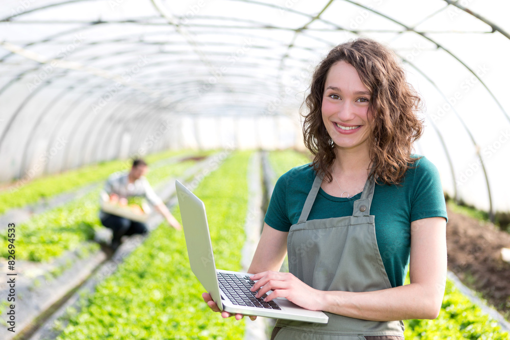 Wall mural portrait of an attractive farmer in a greenhouse using laptop