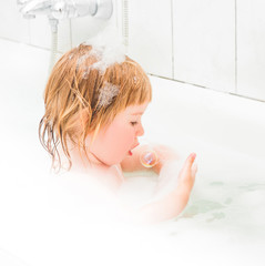 Naklejka premium cute two year old baby bathes in a bath with foam 