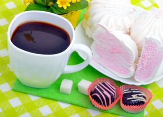 Cup of coffee with marshmallows and chocolate candies on a green