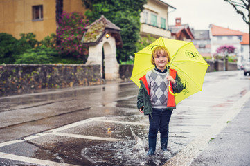 Fototapeta na wymiar Little boy with umbrella playing in the puddle