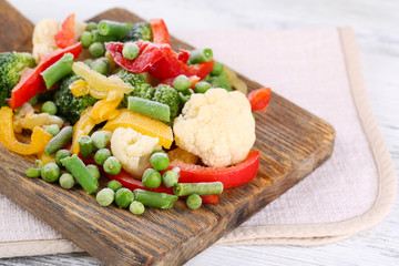 Frozen vegetables on cutting board, on napkin, on wooden table background