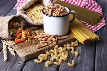 Different types of pasta in containers on wooden background