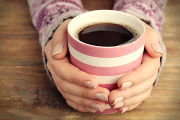 Female hands holding cup of coffee on wooden background