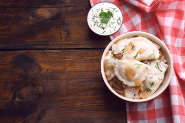 Tasty dumplings with fried onion in brown bowl, on wooden background