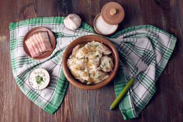 Fried dumplings with onion and bacon in frying pan, on wooden table background