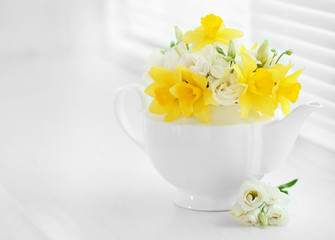 Beautiful bouquet of yellow daffodils and roses in teapot on windowsill