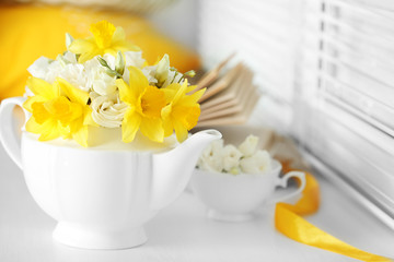 Beautiful bouquet of yellow daffodils and roses in teapot on windowsill