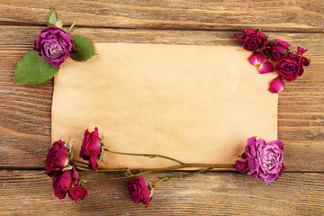 Dried roses on sheet of paper on wooden table, top view