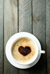 Cup of cappuccino with heart of cocoa on wooden table