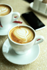 Cups of cappuccino with heart on foam on table in cafe