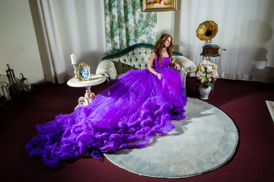 Woman in a luxury, long purple dress sitting on the couch