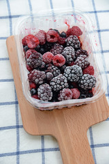 mixed berries on wooden plate with table cloth as background.