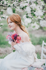 Young woman in vintage wedding dress posing in blooming garden
