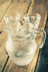 Glass pitcher of water and glass on wooden table.