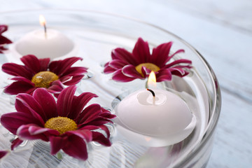 Bowl of spa water with flowers and candles on wooden table, closeup