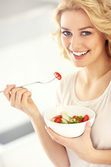 Young woman eating salad in the kitchen