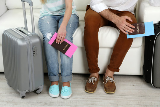 Legs of young happy couple with baggage and tickets, sitting on sofa