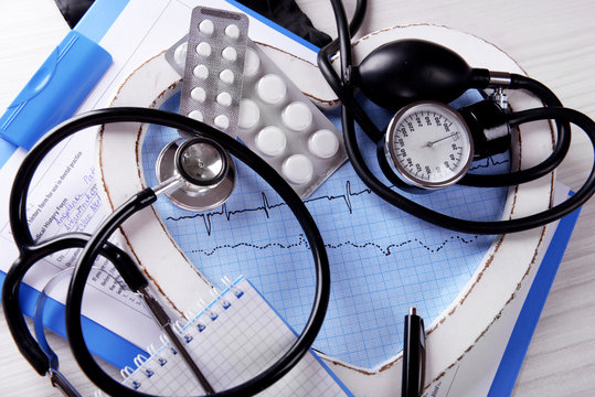 Cardiogram with stethoscope and pills on table, closeup