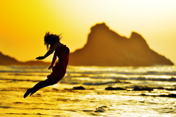 young woman jumping on the beach in summer evening