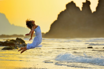 young woman jumping on the beach in summer evening