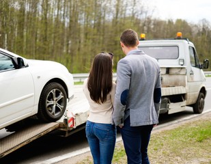 Couple near tow-truck picking up broken car