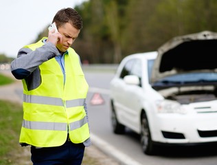Man calling car towing service on a highway roadside