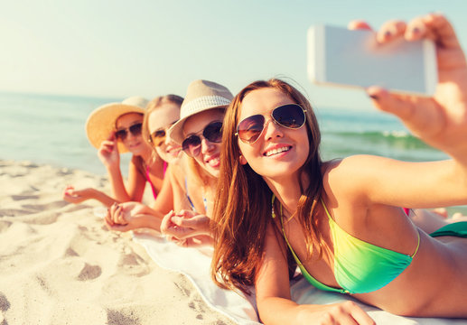 group of smiling women with smartphone on beach