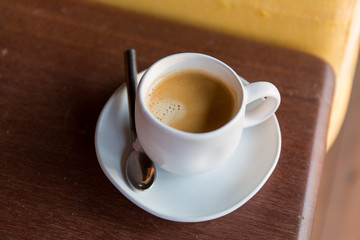 cup of black coffee with spoon and saucer on table