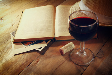 Red wine glass and old book on wooden table at sunset burst