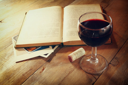 Red wine glass and old book on wooden table at sunset burst